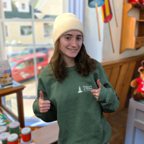 A wilbur's employee giving two thumbs up while wearing the "maine mud" crewneck design in green.